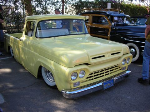 1998 Ford Crown Victoria - A classic yellow pickup truck is parked next to a wood-paneled station wagon at an outdoor event.