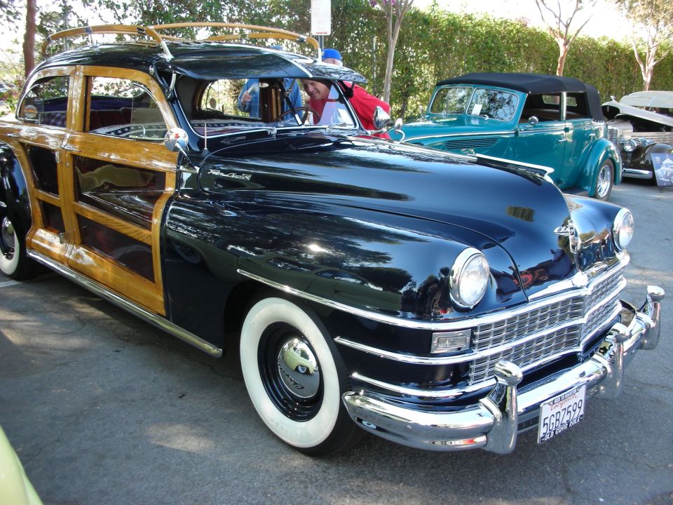 Dark blue woodie wagon with chrome grille and whitewall tires. Another convertible is parked behind it