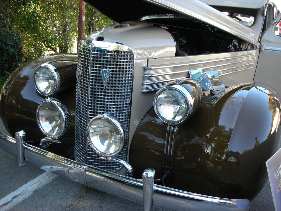 Front view of a vintage car with a large chrome grille and dual headlights. Hood is open