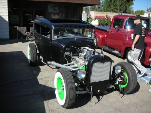 1998 Ford Crown Victoria - A custom hot rod sedan is parked next to a vintage red pickup truck outside a building.