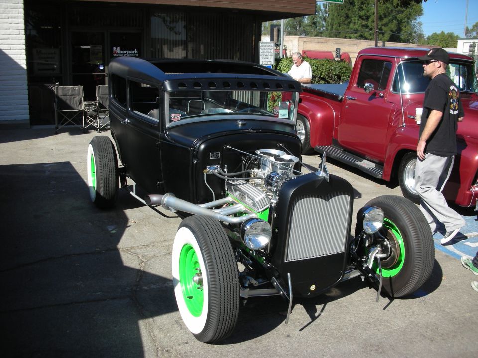 Black hot rod sedan with exposed engine and green wheels parked next to a red pickup truck
