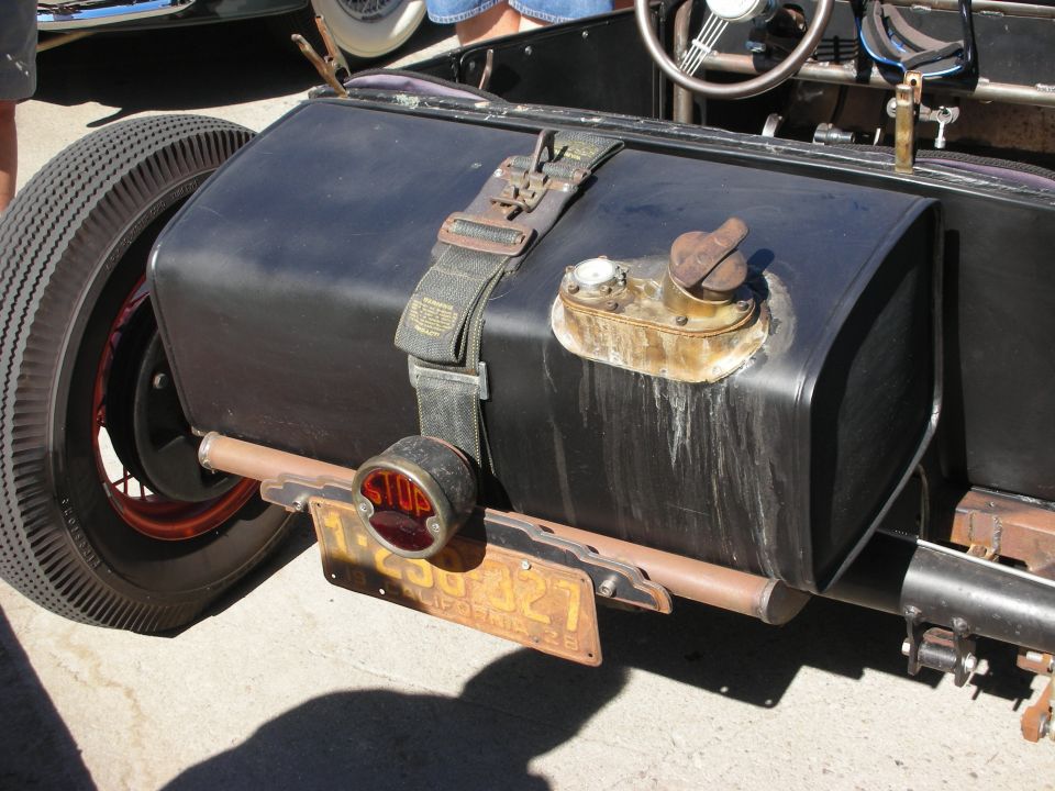 Vintage car fuel tank with strap, stop light, and license plate. Another car is visible in the background
