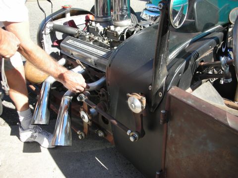 1998 Ford Crown Victoria - A person is adjusting the exhaust system on a heavily modified hot rod with a prominent V8 engine.