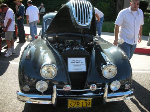 1998 Ford Crown Victoria - A 1956 Jaguar XK140 MC is displayed with its hood open, revealing the engine and a descriptive plaque.