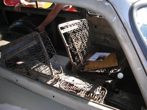 1998 Ford Crown Victoria - The interior of a car shows exposed seat springs and a white shift knob, with a person reaching into the back.