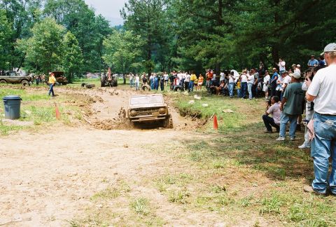 1972 Ford Bronco - A Jeep CJ-5 navigates a muddy obstacle course as a crowd observes the event.