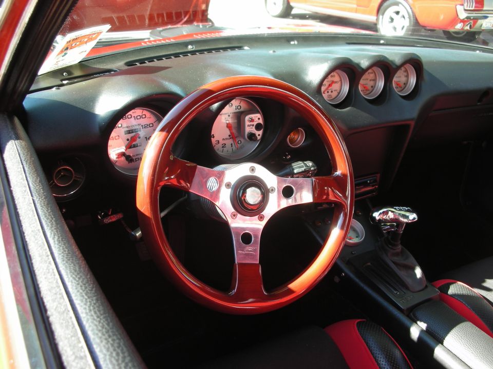 Car interior with a wooden steering wheel, aftermarket gauges, and red and black seats