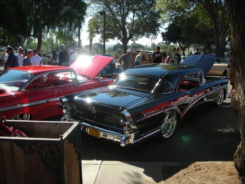 1998 Ford Crown Victoria - Two vintage cars are displayed at an outdoor event, with people milling around in the background.