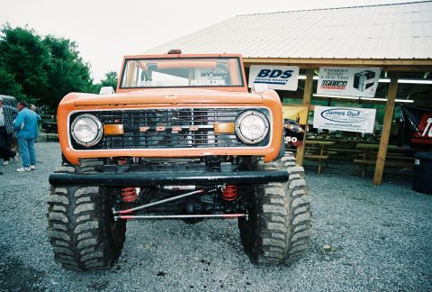 1972 Ford Bronco - A lifted 1972 Ford Bronco with oversized tires is parked in front of a building with various signs.