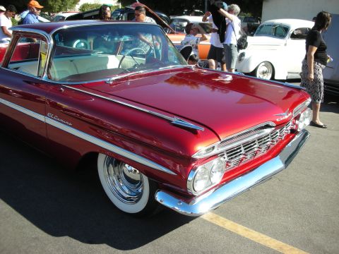 1998 Ford Crown Victoria - Shiny red 1959 Chevrolet El Camino on display at a car show, with other vehicles in the background.