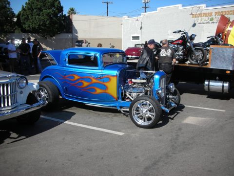 1998 Ford Crown Victoria - A custom blue hot rod with flame graphics is displayed at an outdoor event, with other vehicles present.