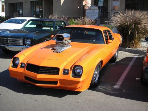 1998 Ford Crown Victoria - A bright orange muscle car with a large supercharger protruding from the hood is parked in a lot.