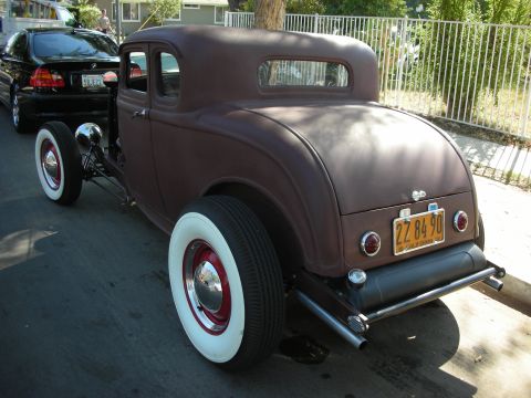 1998 Ford Crown Victoria - A brown hot rod coupe is parked on a street next to a black sedan.