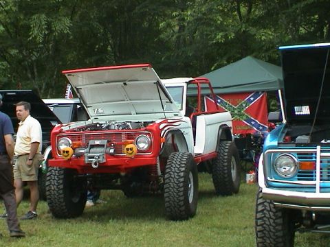 1972 Ford Bronco - A red and white 1972 Ford Bronco with flame decals and a winch is parked on grass, with another vehicle visible to the right.
