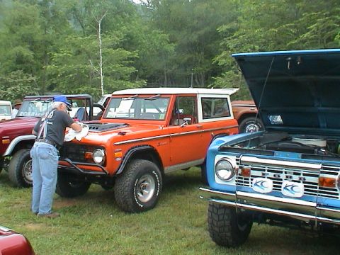 1972 Ford Bronco - A man polishes the hood of an orange Ford Bronco, with other Broncos parked nearby.