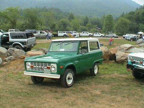 1972 Ford Bronco - A green 1970 Ford Bronco is parked in a field with several other vehicles and trees in the background.