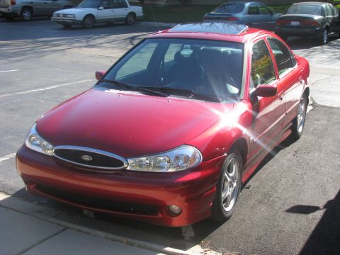 1998 Ford Contour - Front 3/4 view of a red 1998 Ford Contour sedan parked outdoors with other vehicles nearby.