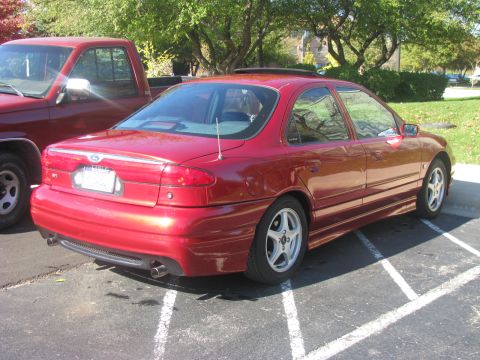 1998 Ford Contour - A red 1998 Ford Contour sedan is parked next to a red pickup truck.