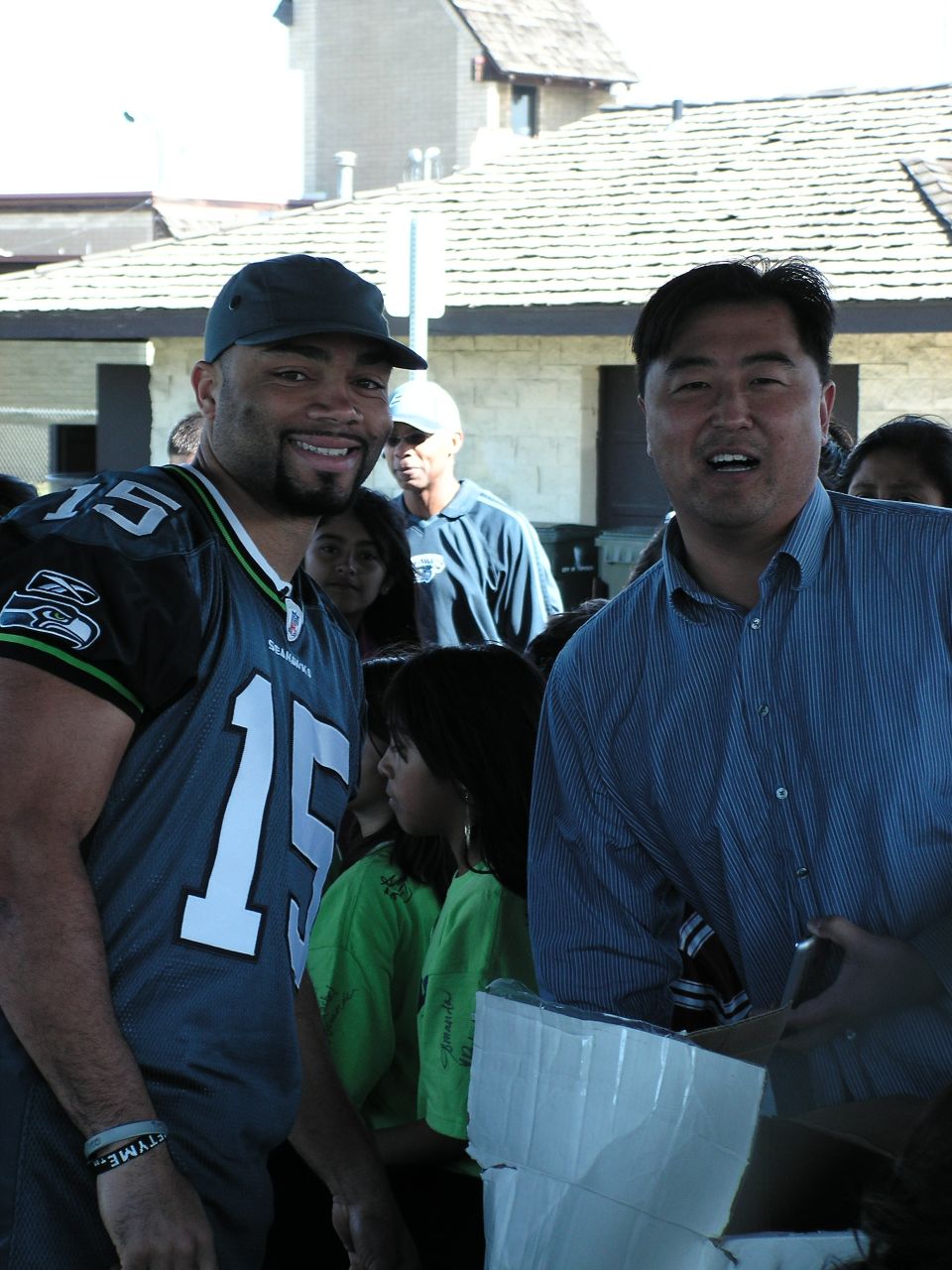 Man in Seahawks jersey and another man smile at the camera, with people behind them