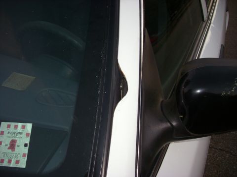 2001 Ford Crown Victoria - A close-up view of a car's side mirror and door frame reveals a dent and a Mississippi inspection sticker on the windshield.