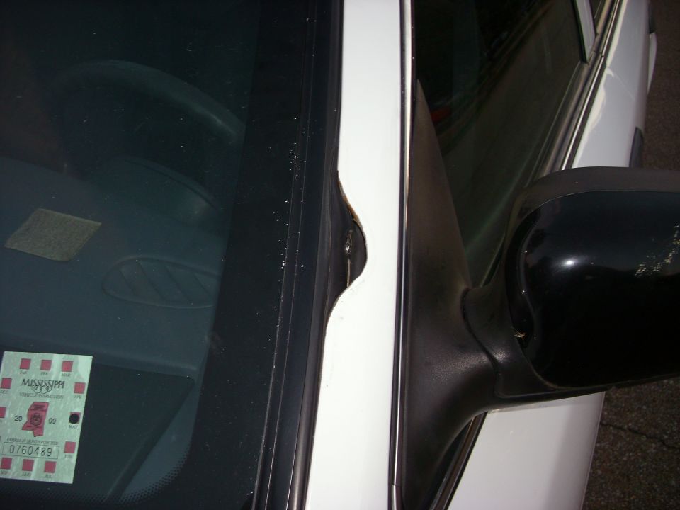 White car door frame with dent, black side mirror, and Mississippi inspection sticker on windshield