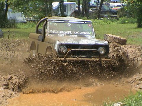 1972 Ford Bronco - A 1972 Ford Bronco navigates a muddy obstacle course, kicking up a large spray of water and dirt.