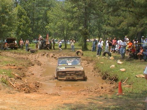 1972 Ford Bronco - Off-road vehicle struggling in a mud pit during an event, with onlookers gathered.