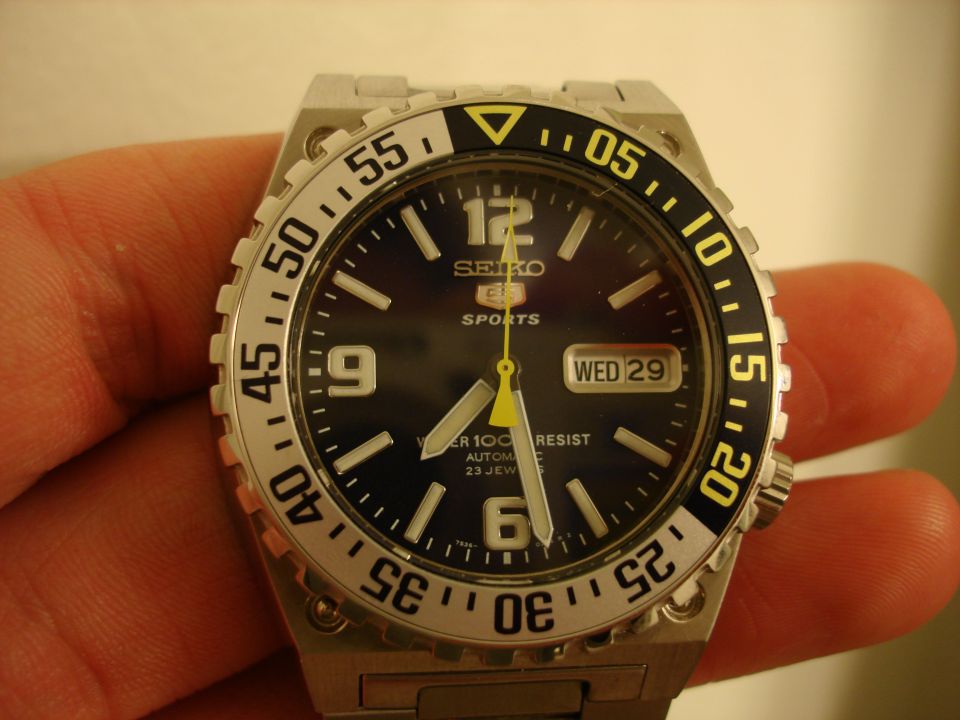 Seiko 5 Sports watch with black dial, yellow accents, and day/date window
