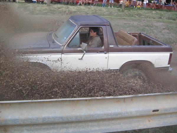 1982 Ford Bronco driving through mud, driver visible inside