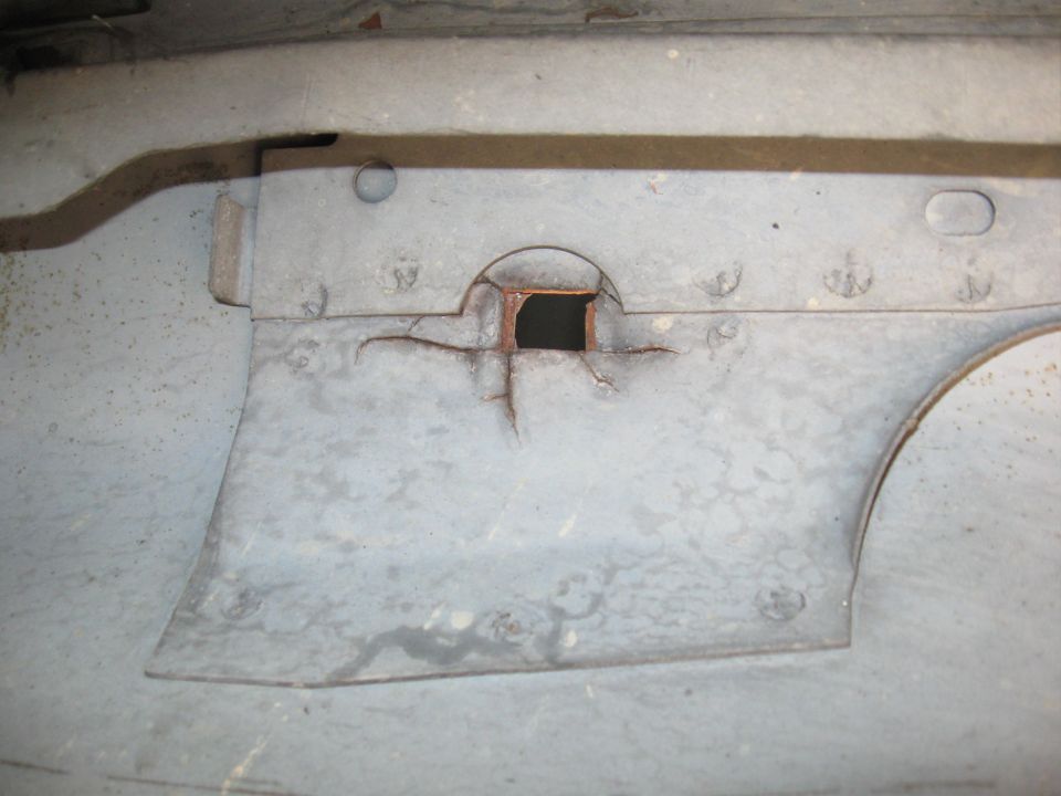 Rusted metal panel with a square opening and cracks, showing rivets and a curved edge