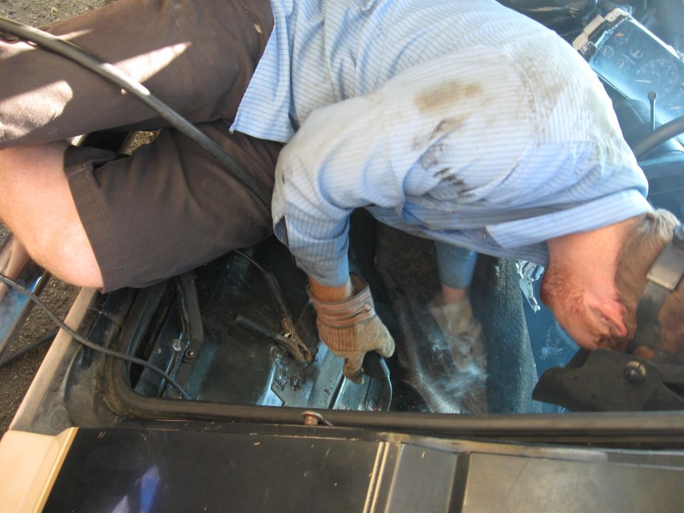Person wearing gloves and a blue striped shirt working on the floor of a vehicle interior