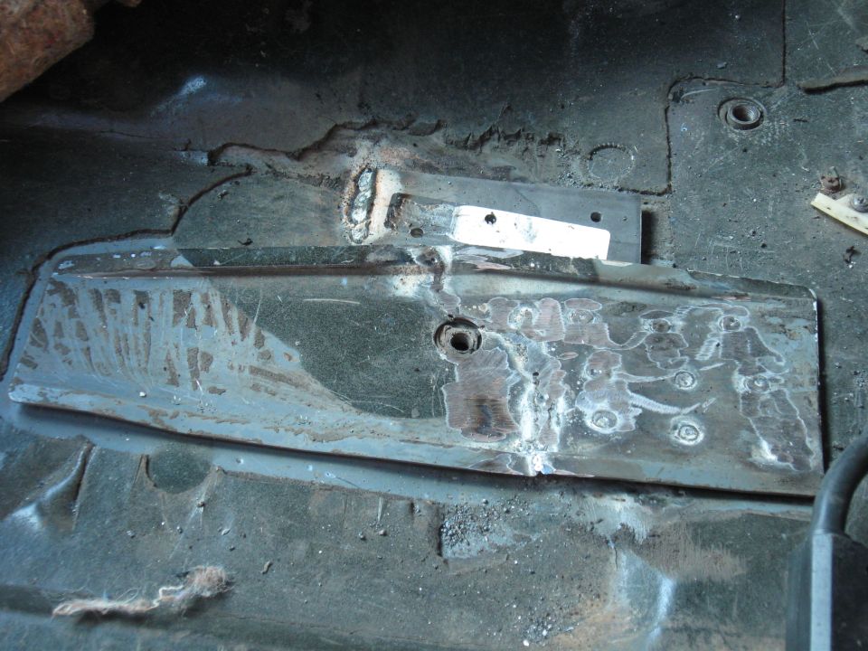 Close-up of a vehicle's floor pan with metal patches and welds, indicating repair work