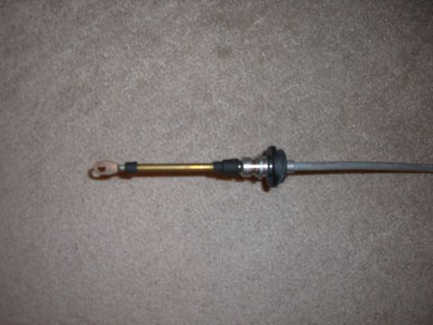 1988 Ford Bronco - A shift cable assembly, a brass-colored housing and metal components, is shown laid out on a carpeted surface.