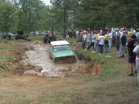 1972 Ford Bronco - A green off-road vehicle navigates a muddy track while a crowd observes the event.