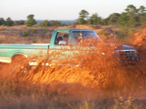 2008 International School Bus - A green pickup truck navigates a muddy terrain, sending up a spray of dirt.