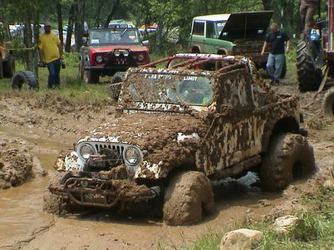 1972 Ford Bronco - Multiple off-road vehicles navigate a muddy terrain, with one prominently stuck in a mud pit.
