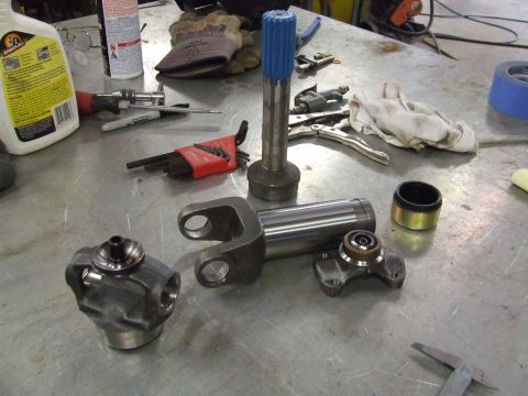 1967 Ford Bronco - Various driveshaft components, including U-joints and a yoke, are arranged on a metal surface alongside tools and shop supplies.