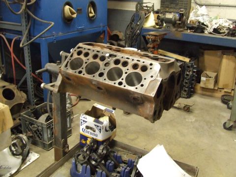 1967 Ford Bronco - Engine block on a stand in a workshop setting, surrounded by tools and parts.