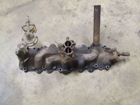 1967 Ford Bronco - Intake manifold assembly with a two-barrel carburetor and fuel pump attached, resting on a concrete surface.