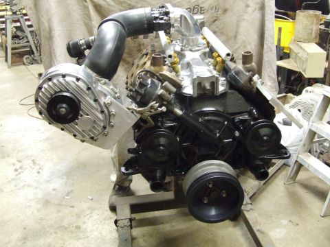 1967 Ford Bronco - A V8 engine with a prominent supercharger is mounted on a stand in a workshop setting.