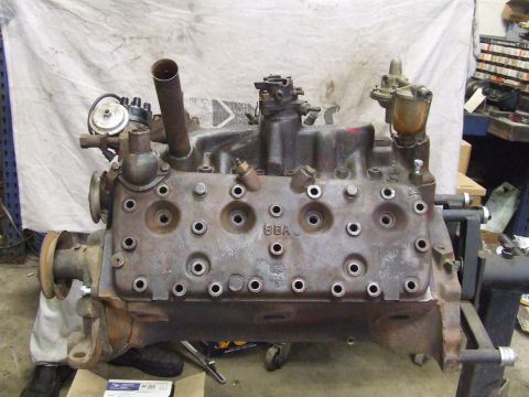 1967 Ford Bronco - A Ford Flathead V8 engine is mounted on an engine stand, showing its front cylinder bank and manifold details.