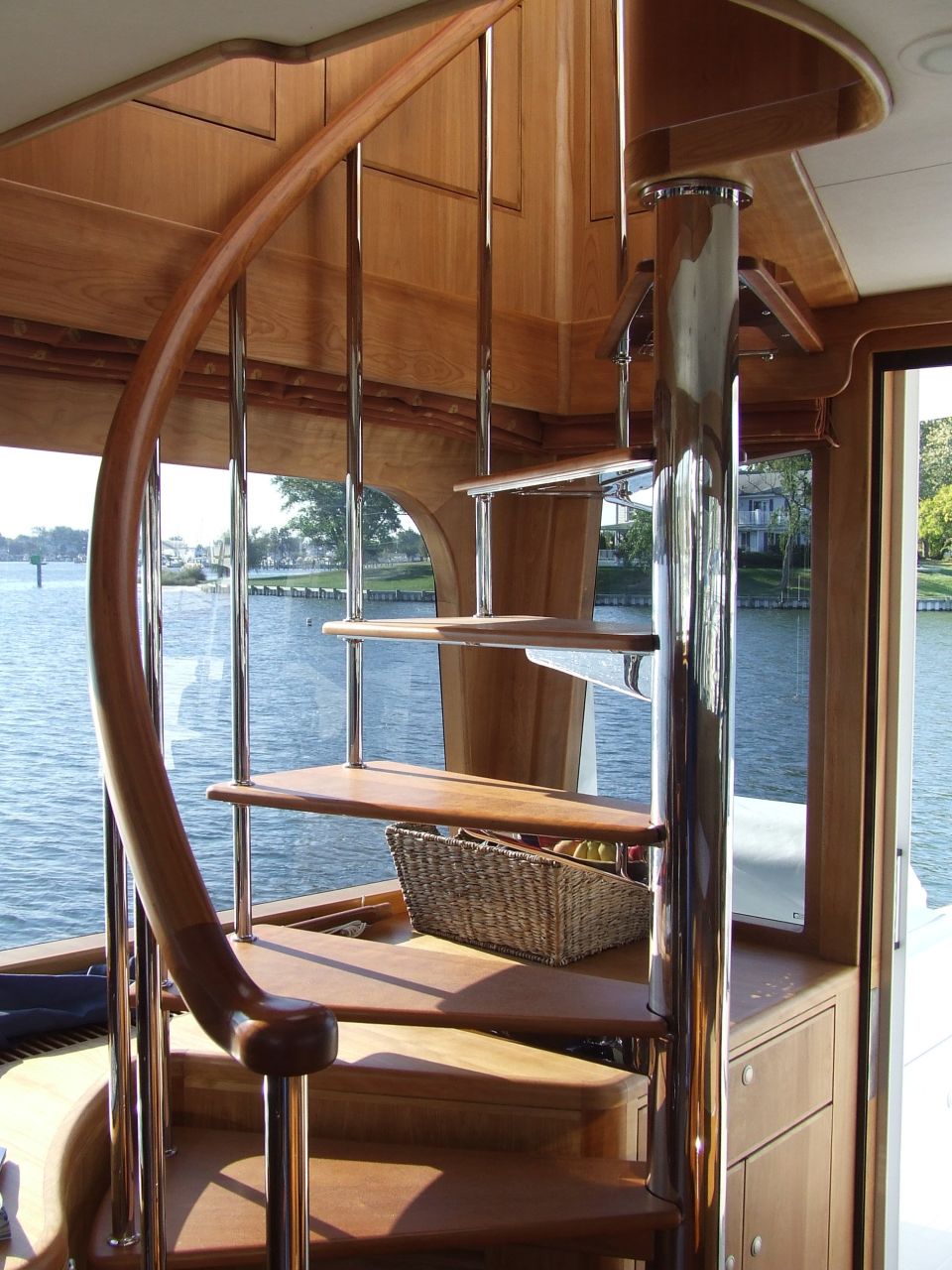 Wooden spiral staircase with chrome railings inside a boat, overlooking water