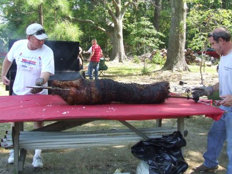 1976 Ford F-150 - A whole animal is being roasted on a spit over a fire pit at an outdoor gathering.
