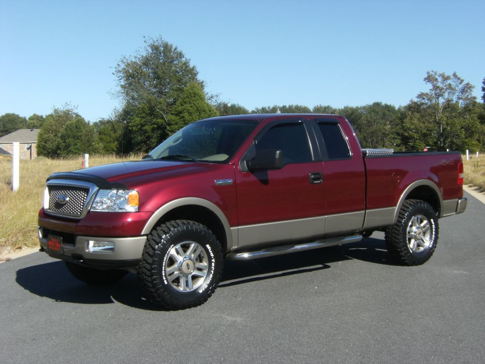 Maroon Ford F-150 extended-cab pickup, lifted with off-road tires, 3/4 front view