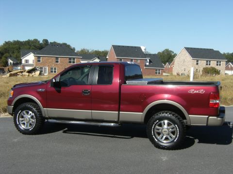 2005 Ford F-150 - Driver-side profile of a maroon and tan two-tone Ford F-150 extended-cab pickup parked on asphalt in a new housing development, wearing BFG…