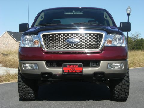 2005 Ford F-150 - Head-on front view of a dark-red Ford F-150 with tan two-tone lower bumpers, a chrome honeycomb grille with blue Ford oval, a smoked hood d…