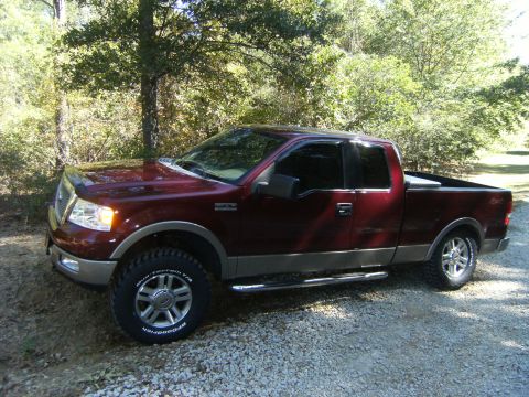 2005 Ford F-150 - This maroon Ford F-150 pickup truck is parked on a gravel surface with trees in the background.