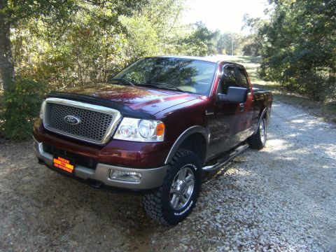 2005 Ford F-150 - A maroon Ford F-150 pickup truck is parked on a gravel road surrounded by trees.
