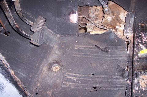 1976 Ford Bronco - Close-up of a vehicle's interior floor showing extensive rust and damage around the pedals and transmission tunnel.