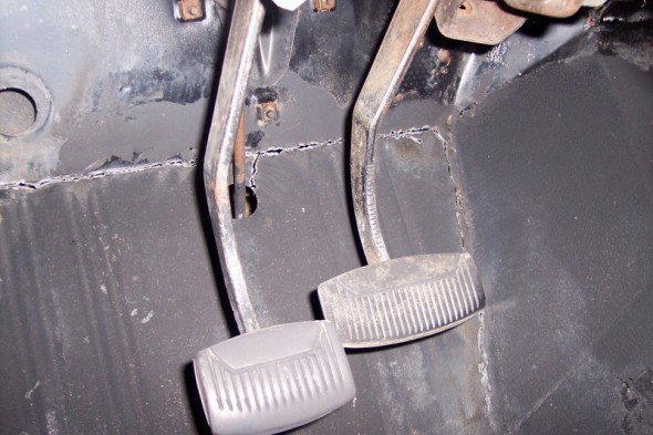 Close-up of floor pedals and rusted metal in a vehicle